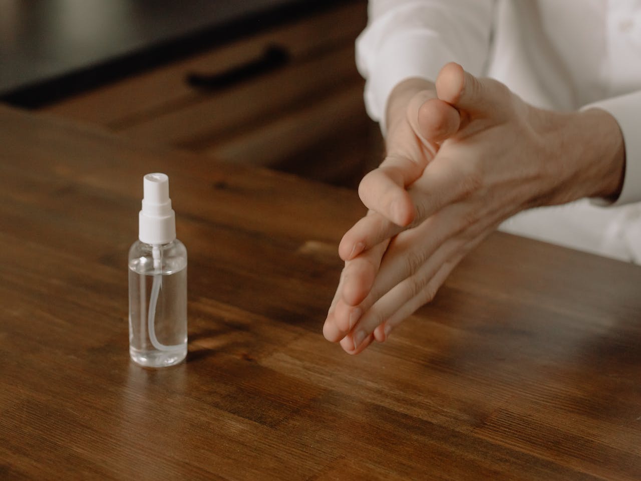 Close-up of hands applying sanitizer on a wooden table, emphasizing hygiene and health.